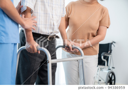 Contented senior man was helped on folding walker by his wife and caregiver. Contented senior man was helped on folding walker by his wife and caregiver. 94386959