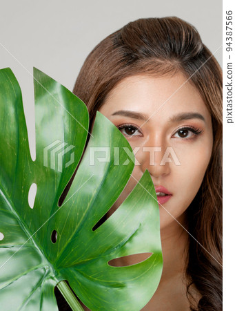 Closeup young ardent woman with healthy skin holding green leaf near her face. 94387566