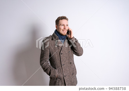 A young man in an autumn coat is talking on the phone emotionally against A young man in an autumn coat is talking on the phone emotionally against 94388738