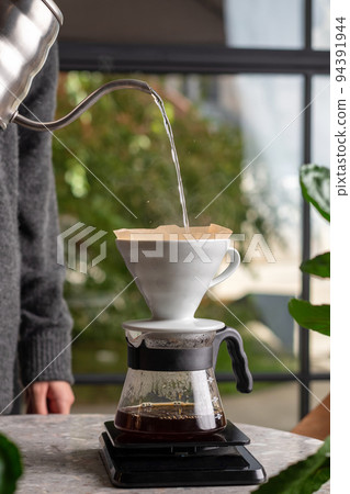 Barista is making drip brewing, filtered coffee, or pour over coffee with hot water and filter paper in coffee shop 94391944