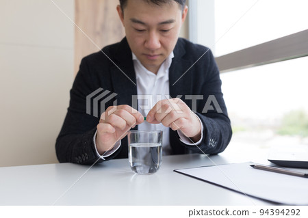 Close up of businessman in the office holding pills and glass of fresh water, taking medicine for headache, abdominal pain or taking vitamins, healthcare concept 94394292