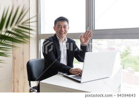 Successful Asian businessman, in a black business suit, works on a laptop, in a stylish office explains a new business strategy via video link Successful Asian businessman, in a black business suit, works on a laptop, in a stylish office explains a new business strategy via video link 94394643