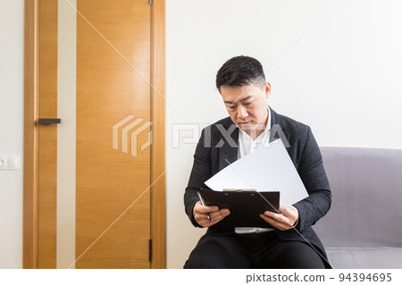 Young successful Asian man, waiting for a job interview, in the waiting room of the office center, sitting on a chair near the reception of the office center 94394695