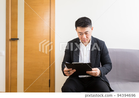 Young successful Asian man, waiting for a job interview, in the waiting room of the office center, sitting on a chair near the reception of the office center Young successful Asian man, waiting for a job interview, in the waiting room of the office center, sitting on a chair near the reception of the office center 94394696