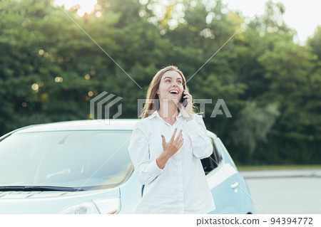 Beautiful young woman bought a new car, smiling and happy, talking on the phone, sharing with friends the news about buying a car Beautiful young woman bought a new car, smiling and happy, talking on the phone, sharing with friends the news about buying a car 94394772