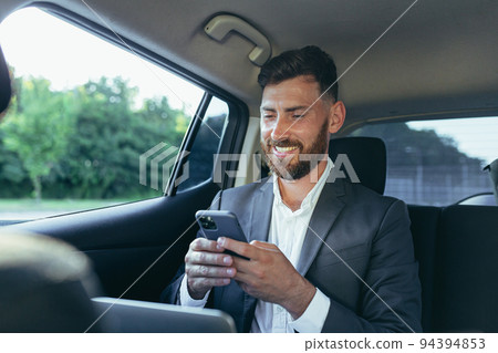 Happy and successful male businessman car passenger reads the news from the phone, rejoices in the victory and the news received Happy and successful male businessman car passenger reads the news from the phone, rejoices in the victory and the news received 94394853