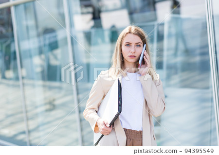 Young beautiful woman talking on a cell phone near the office, a businesswoman on a lunch break Young beautiful woman talking on a cell phone near the office, a businesswoman on a lunch break 94395549