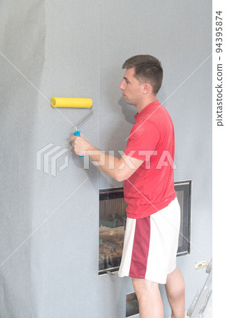 a worker glues wallpaper on the wall with a fireplace using a rubber roller. a worker glues wallpaper on the wall with a fireplace using a rubber roller. 94395874