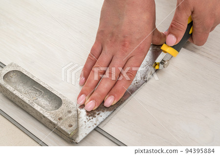 Woman master cuts quartz vinyl floor with a stationery knife, floor installation. 94395884