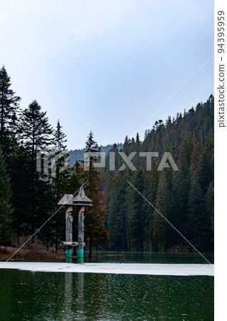 Alpine lake Synevyr, wooden statues near the lake, a tourist place in Ukraine, ice on the lake. 94395959
