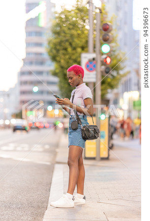 Afro young woman standing on the street using the mobile Afro young woman standing on the street using the mobile 94396673