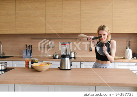 Woman plays in kitchen like she is warrior with sword and shield. 94397725