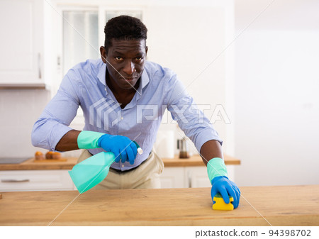 Aframerican guy in gloves washes kitchen table with detergent Aframerican guy in gloves washes kitchen table with detergent 94398702