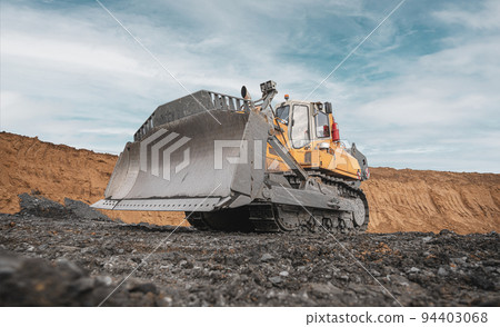 Yellow excavator in career moves overburden. Bulldozer combs the ground, with the bright sun and nice blue sky in the background 94403068