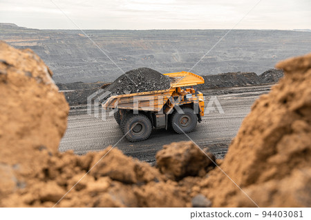 Large quarry dump truck. Big yellow mining truck at work site. Loading coal into body truck. Production useful minerals. Mining truck mining machinery to transport coal from open-pit production 94403081