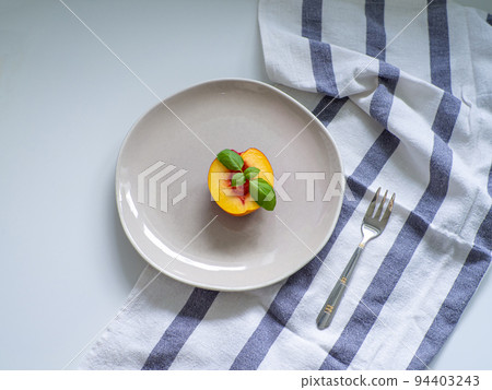 nectarine and green basil on the beige plate with fork on white table nectarine and green basil on the beige plate with fork on white table 94403243