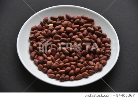 Peanuts on a white plate on a black background. Delicious nutty breakfast. Peanuts on a white plate on a black background. Delicious nutty breakfast. 94403367