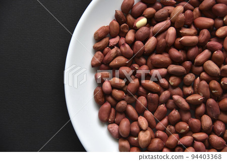 Peanuts on a white plate on a black background. Delicious nutty breakfast. Peanuts on a white plate on a black background. Delicious nutty breakfast. 94403368