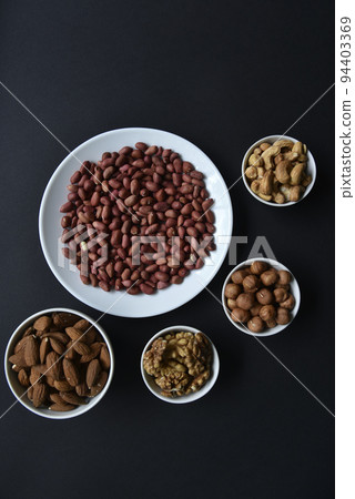 Peanuts on a white plate on a black background. Delicious walnut breakfast with walnuts, cashews and almonds. Peanuts on a white plate on a black background. Delicious walnut breakfast with walnuts, cashews and almonds. 94403369