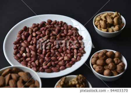 Peanuts on a white plate on a black background. Delicious walnut breakfast with walnuts, cashews and almonds. 94403370