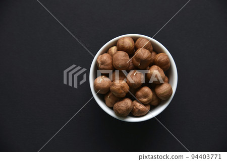 Delicious hazelnuts in a ceramic bowl on a black background. Delicious breakfast of nuts. 94403771