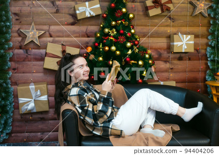 A young girl with a mischievous smile reads a book lying on the sofa on New Year's Eve A young girl with a mischievous smile reads a book lying on the sofa on New Year's Eve 94404206