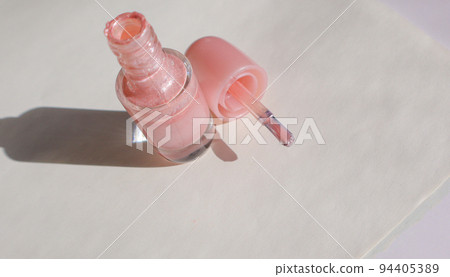 An open bottle with pink nail polish and a brush next to it on a white surface with a shadow, the concept of fashionable beauty 94405389