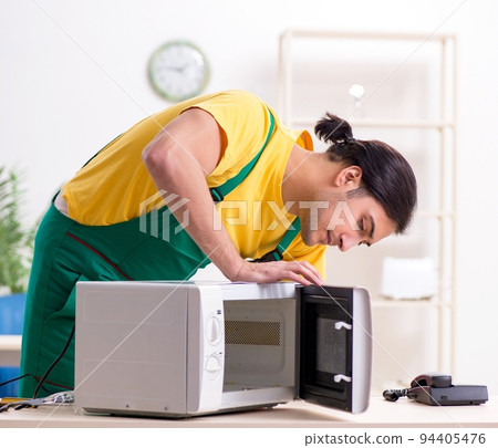 Young repairman repairing microwave in service centre Young repairman repairing microwave in service centre 94405476