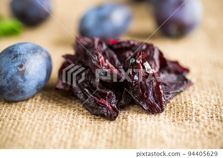 Dried prunes in a spoon on a burlap tablecloth against a background of fresh plums. Dried prunes in a spoon on a burlap tablecloth against a background of fresh plums. 94405629