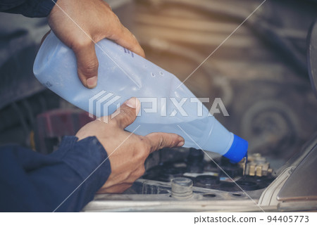 Car Mechanic man hands pouring Deionized purified Distilled water for car battery mechanical service. Close up hands man hold Deionized Distilled liquid water bottle at garage auto mobile car service 94405773