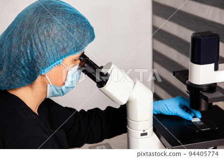 Female scientist looking at slides with patient samples using an inverted microscope in the laboratory. 94405774