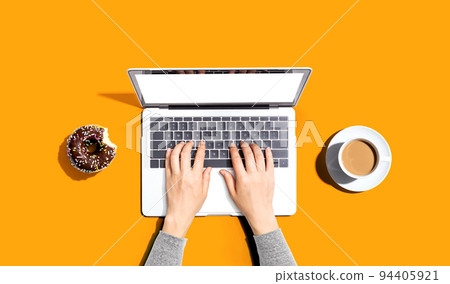 Person using a laptop computer with a donut and a cup of coffee Person using a laptop computer with a donut and a cup of coffee 94405921