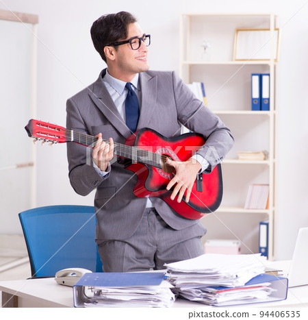 Young handsome businessman playing guitar in the office Young handsome businessman playing guitar in the office 94406535