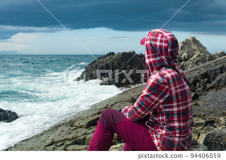 traveler sits on the shore of a stormy sea, on a natural pavement made of columnar granite traveler sits on the shore of a stormy sea, on a natural pavement made of columnar granite 94406859