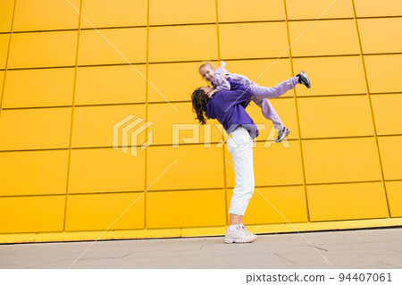 Woman in purple hoody have fun with cute girl 4-5 years old. Mommy and little daughter on yellow mall wall background. Childhood concept of love for family and fatherhood on Mother's Day 94407061