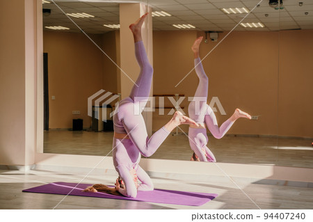 A slender peaceful positive Caucasian fitness model in a purple suit stands on her head on a purple rug. A woman performs S hirshasana. The concept of body positivity, healthy lifestyle 94407240