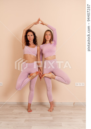 Two beautiful women cook doing yoga, sports together in the gym. Dressed in pink suits. The concept of grace and beauty of the body. 94407287