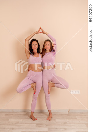 Two beautiful women cook doing yoga, sports together in the gym. Dressed in pink suits. The concept of grace and beauty of the body. 94407290