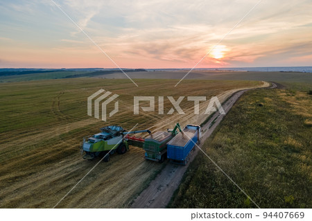 Aerial view of combine harvester unloading grain in cargo trailer working during harvesting season on large ripe wheat field. Agriculture and transportation of raw farm products concept Aerial view of combine harvester unloading grain in cargo trailer working during harvesting season on large ripe wheat field. Agriculture and transportation of raw farm products concept 94407669