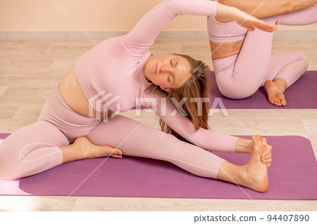 Two beautiful women cook doing yoga, sports together in the gym. Dressed in pink suits. The concept of grace and beauty of the body. 94407890