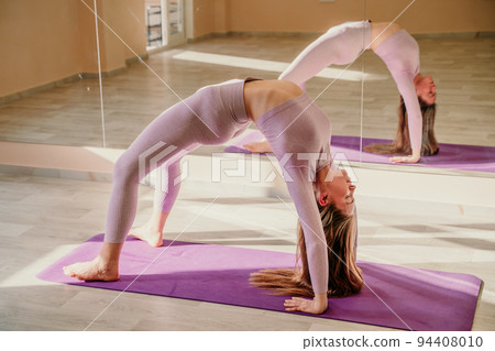 View from above. A beautiful young woman in pink sportswear is engaged in yoga, sports in the hall on a purple rug. Yoga, sport and healthy concept. 94408010