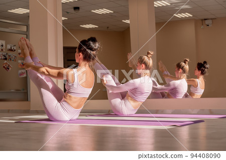 Two beautiful women cook doing yoga, sports together in the gym. Dressed in pink suits. The concept of grace and beauty of the body. 94408090