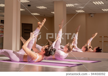 Two beautiful women cook doing yoga, sports together in the gym. Dressed in pink suits. The concept of grace and beauty of the body. 94408092