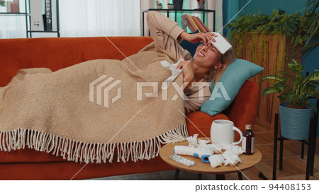 Sick ill woman suffering from cold or allergy lying on home sofa sneezes wipes snot into napkin Sick ill woman suffering from cold or allergy lying on home sofa sneezes wipes snot into napkin 94408153