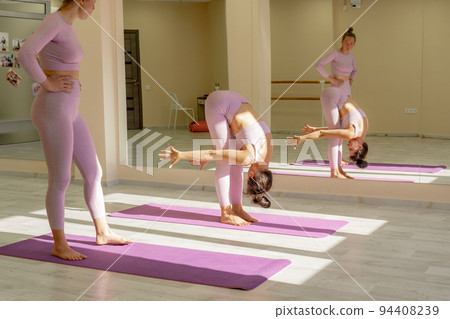 Two beautiful women cook doing yoga, sports together in the gym. Dressed in pink suits. The concept of grace and beauty of the body. 94408239