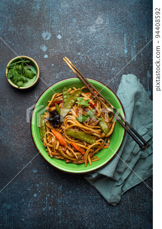Asian stir fry noodles with chicken and veggies in green bowl top view 94408592