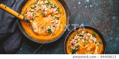 Bowl with pumpkin cream soup with peanuts on dark stone background 94408613