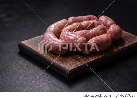 Raw barbecue sausages on a wooden cutting board with spices and herbs Raw barbecue sausages on a wooden cutting board with spices and herbs 94408703