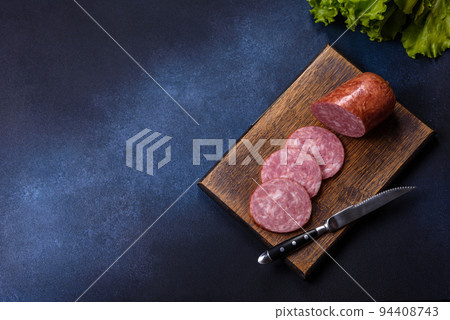 Delicious fresh smoked sausage cut with slices on a wooden cutting board Delicious fresh smoked sausage cut with slices on a wooden cutting board 94408743