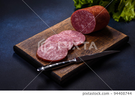 Delicious fresh smoked sausage cut with slices on a wooden cutting board 94408744